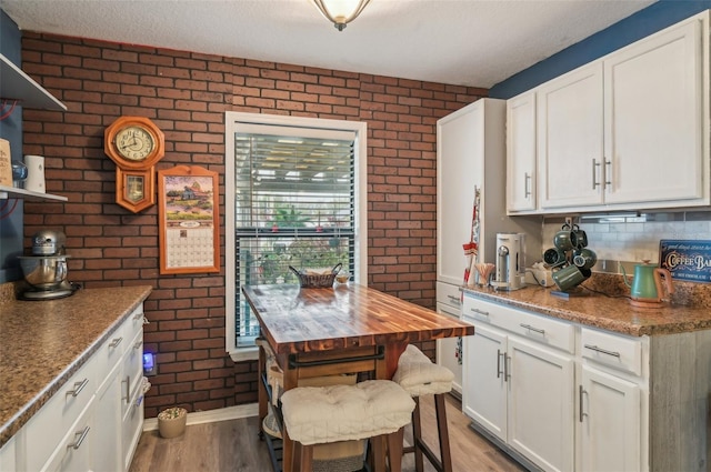 kitchen featuring light wood-style flooring, brick wall, and white cabinetry