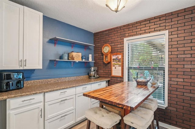 kitchen featuring open shelves, a textured ceiling, white cabinets, and brick wall