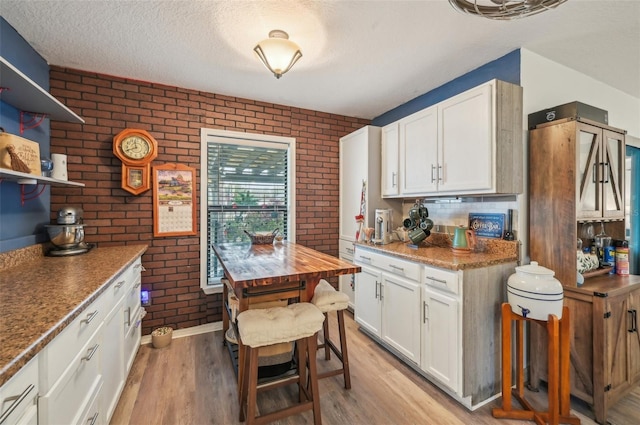 kitchen with light wood-style flooring, brick wall, and white cabinets