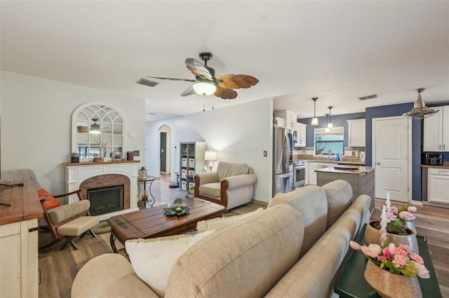 living area with wood finished floors, a brick fireplace, arched walkways, and visible vents