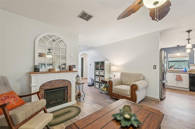 living area with a ceiling fan, a stone fireplace, arched walkways, and visible vents