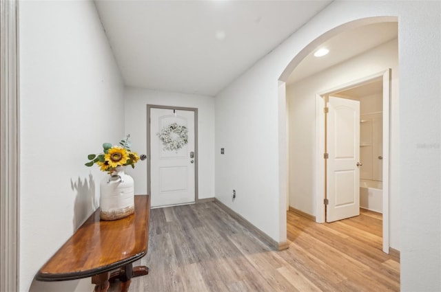 entryway with arched walkways, baseboards, and light wood-style floors