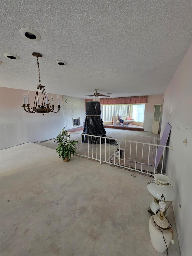 interior space featuring visible vents, a textured ceiling, unfinished concrete floors, and ceiling fan with notable chandelier