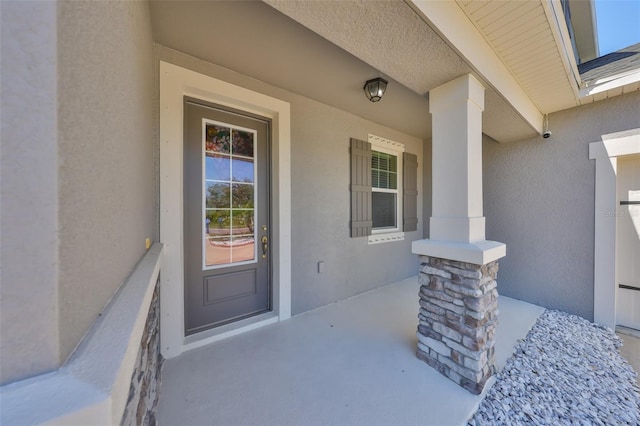 property entrance with stucco siding, a porch, and a shingled roof