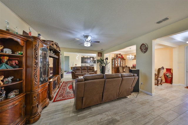 living room featuring visible vents, a textured ceiling, and ceiling fan with notable chandelier