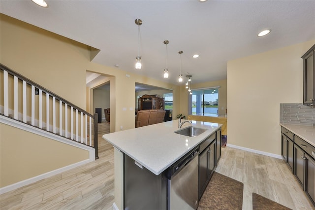 kitchen featuring stainless steel dishwasher, light wood finished floors, backsplash, and a sink