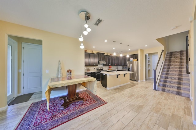 kitchen with visible vents, an island with sink, light countertops, stainless steel refrigerator with ice dispenser, and under cabinet range hood