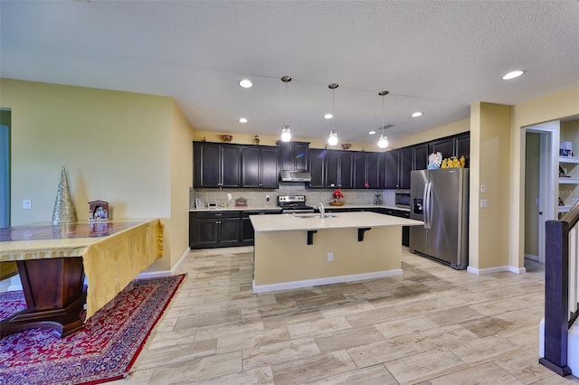 kitchen with under cabinet range hood, a kitchen bar, light countertops, decorative backsplash, and stainless steel appliances