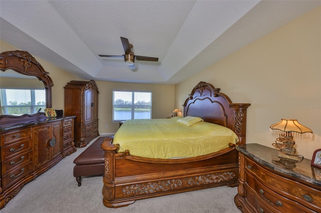 bedroom with ceiling fan, a tray ceiling, and light carpet