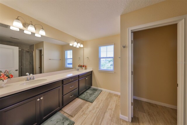 full bath with double vanity, a stall shower, wood finished floors, a textured ceiling, and a sink