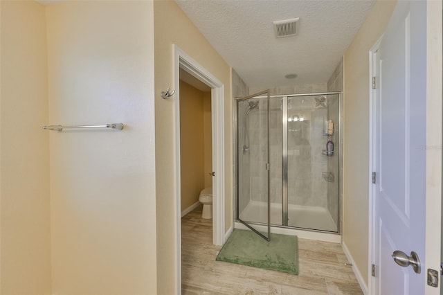 bathroom with visible vents, a shower stall, toilet, wood finished floors, and a textured ceiling