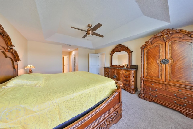 carpeted bedroom with a tray ceiling, visible vents, and ceiling fan