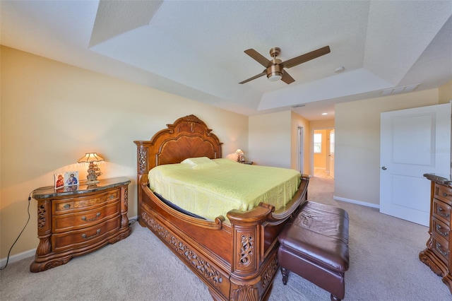 bedroom featuring a ceiling fan, ensuite bathroom, a tray ceiling, carpet floors, and baseboards