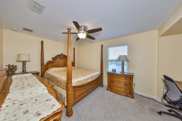 bedroom featuring light carpet, visible vents, a textured ceiling, and a ceiling fan