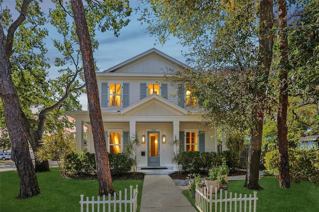 view of front of house featuring board and batten siding, a front lawn, covered porch, and a fenced front yard