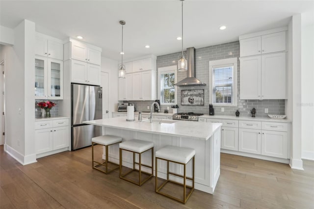 kitchen with a breakfast bar, appliances with stainless steel finishes, white cabinetry, wall chimney exhaust hood, and a sink