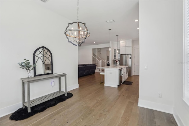 kitchen with a notable chandelier, wood finished floors, open floor plan, white cabinetry, and appliances with stainless steel finishes