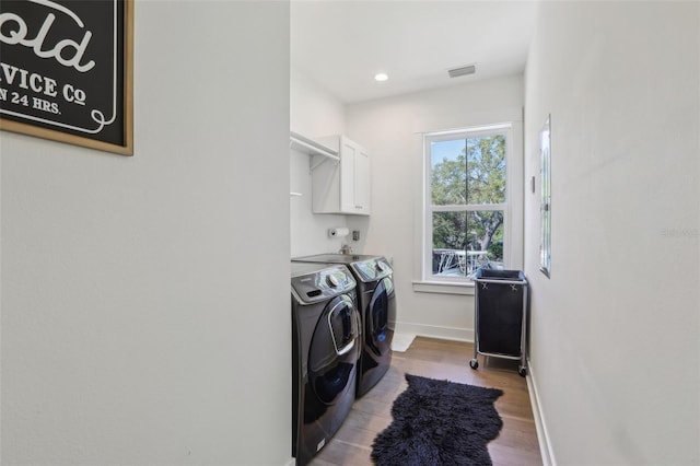 laundry area with wood finished floors, visible vents, baseboards, washing machine and clothes dryer, and cabinet space