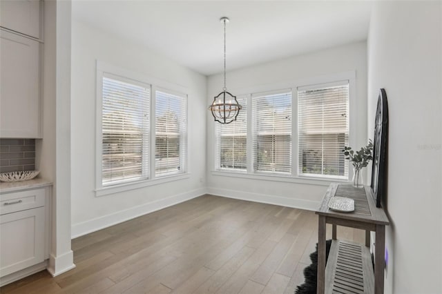 unfurnished dining area with light wood-style flooring, baseboards, and a chandelier