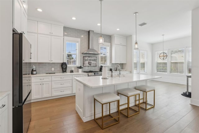 kitchen with tasteful backsplash, white cabinetry, wall chimney range hood, and hardwood / wood-style flooring