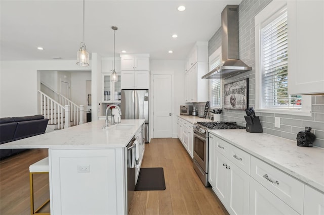 kitchen featuring tasteful backsplash, stainless steel appliances, a kitchen breakfast bar, wall chimney exhaust hood, and light wood-type flooring