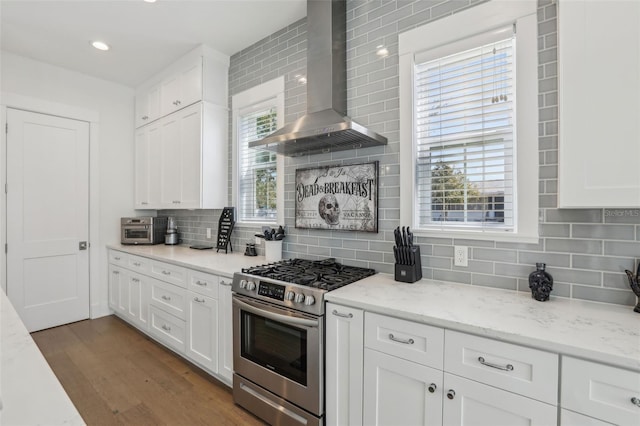 kitchen featuring wall chimney range hood, decorative backsplash, wood finished floors, white cabinets, and gas stove