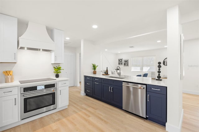 kitchen featuring appliances with stainless steel finishes, white cabinetry, custom range hood, and a sink