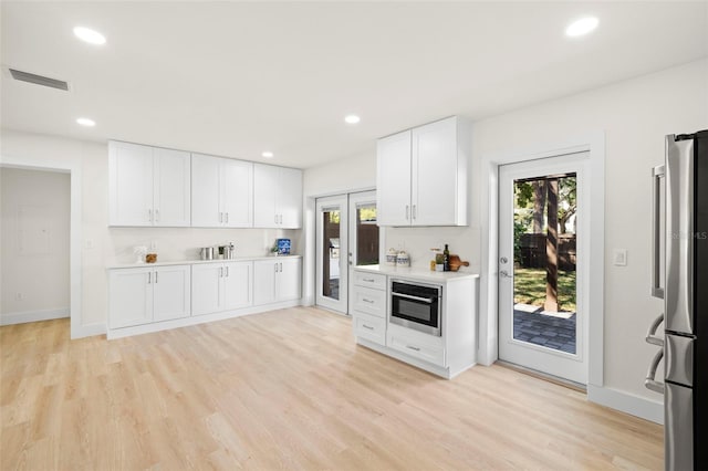 kitchen with visible vents, stainless steel appliances, light countertops, white cabinetry, and light wood-type flooring