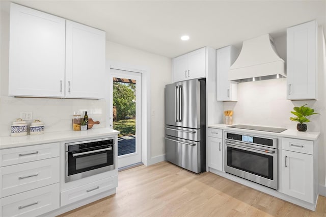 kitchen with light wood finished floors, light countertops, custom range hood, appliances with stainless steel finishes, and white cabinetry