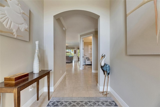 corridor with crown molding, light tile patterned floors, baseboards, and arched walkways