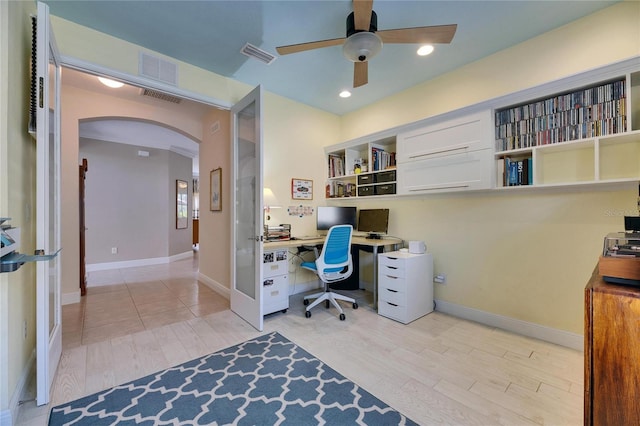 home office with arched walkways, visible vents, light wood-style floors, and ceiling fan