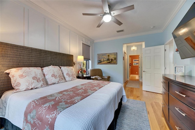 bedroom featuring a ceiling fan, visible vents, crown molding, a decorative wall, and light wood-type flooring