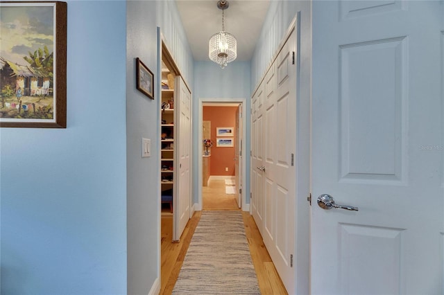 hall featuring a notable chandelier, light wood-type flooring, and baseboards