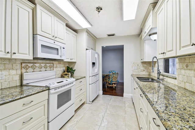 kitchen featuring white appliances, light stone counters, baseboards, visible vents, and a sink