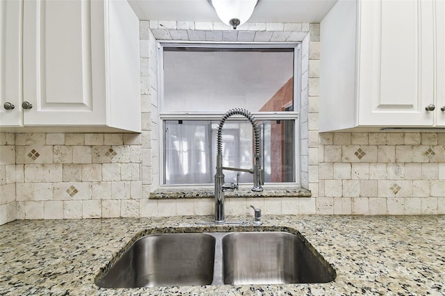 kitchen featuring a sink, light stone countertops, backsplash, and white cabinets