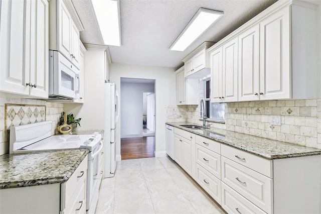 kitchen featuring white appliances, light stone counters, a sink, white cabinets, and tasteful backsplash