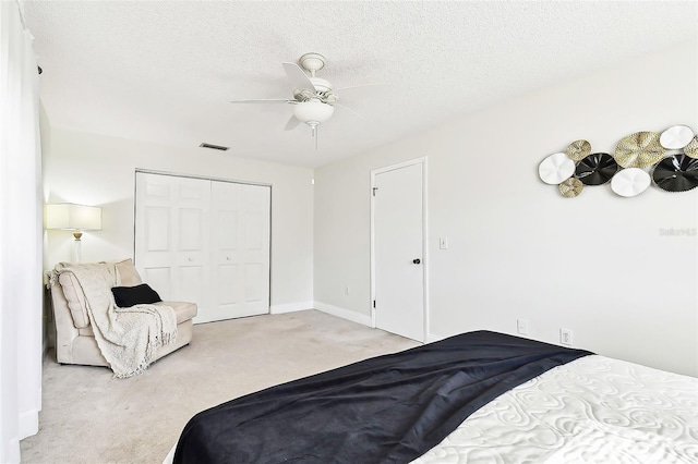 carpeted bedroom featuring visible vents, baseboards, a closet, a textured ceiling, and a ceiling fan
