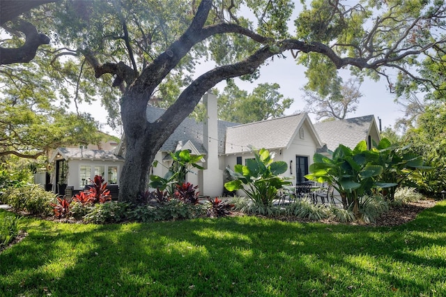 view of home's exterior with stucco siding, a yard, roof with shingles, and a chimney