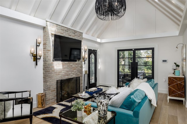 living area featuring wood finished floors, baseboards, beam ceiling, a brick fireplace, and a chandelier