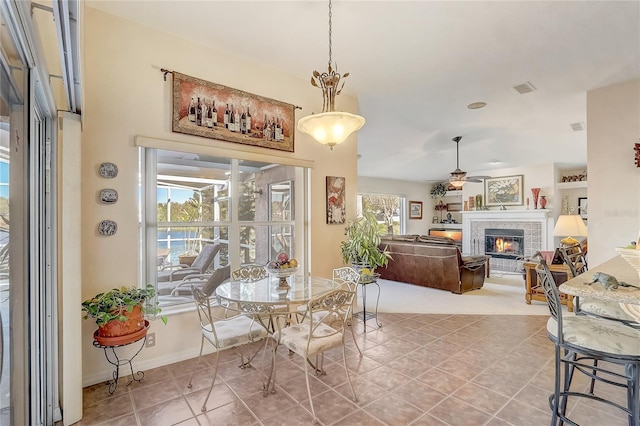 tiled dining space with ceiling fan, visible vents, baseboards, and a glass covered fireplace