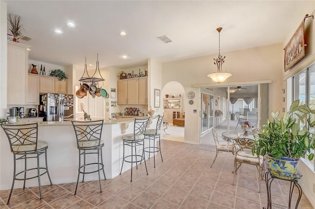 kitchen with a ceiling fan, a peninsula, stainless steel fridge with ice dispenser, arched walkways, and a kitchen bar