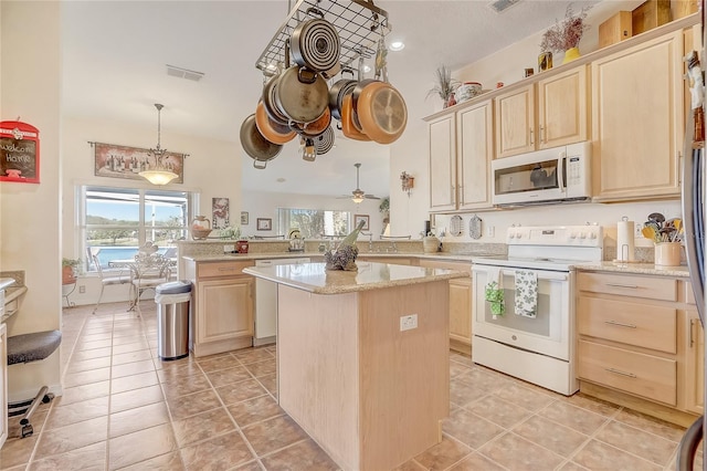 kitchen with a peninsula, white appliances, light brown cabinets, and a wealth of natural light