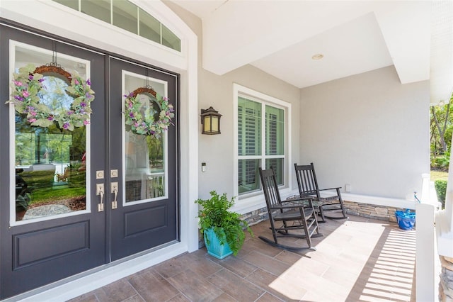 entrance to property featuring covered porch, stucco siding, and french doors