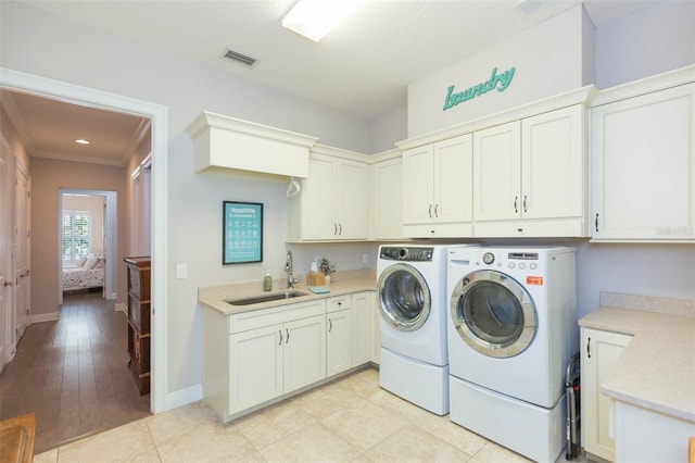 clothes washing area with visible vents, a sink, washing machine and dryer, cabinet space, and baseboards