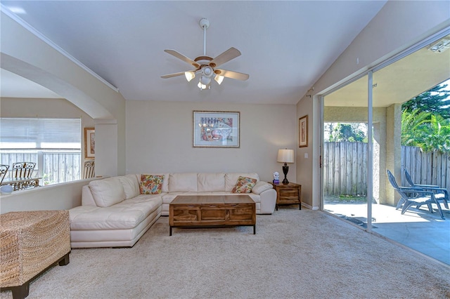 carpeted living room with arched walkways, ceiling fan, ornamental molding, and vaulted ceiling