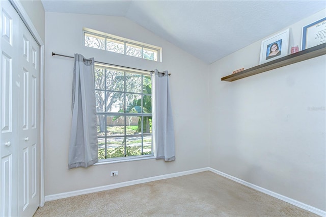 carpeted empty room featuring baseboards and lofted ceiling