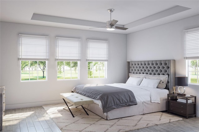 bedroom with a ceiling fan, a tray ceiling, wood finished floors, and baseboards