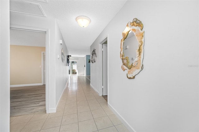 hallway with light tile patterned floors, visible vents, baseboards, and a textured ceiling