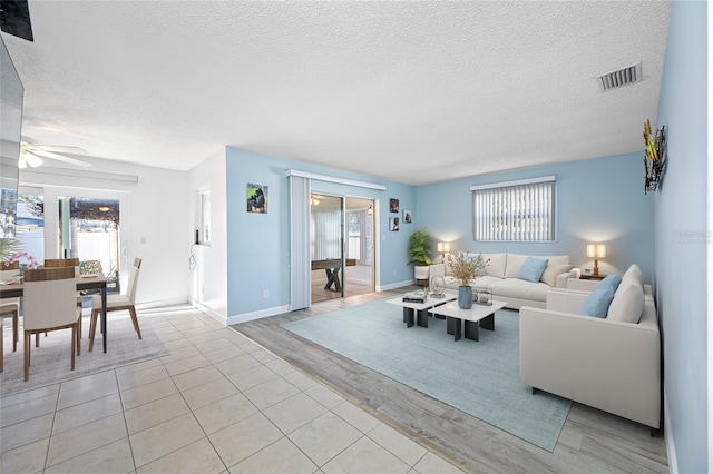 living room featuring visible vents, a textured ceiling, light wood-type flooring, and a ceiling fan