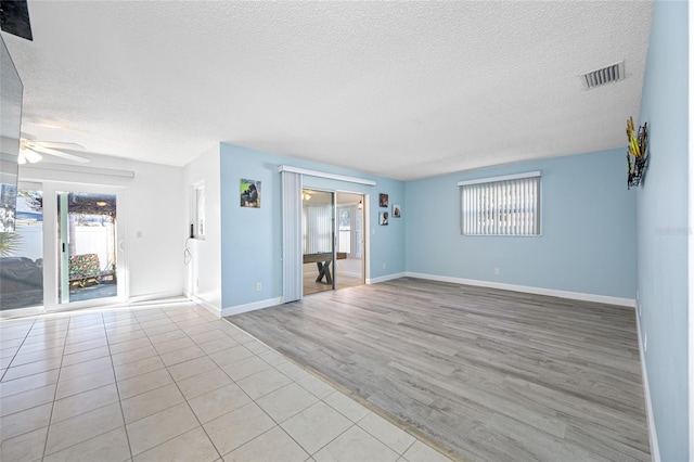 unfurnished living room featuring light wood-type flooring, a ceiling fan, visible vents, and a textured ceiling